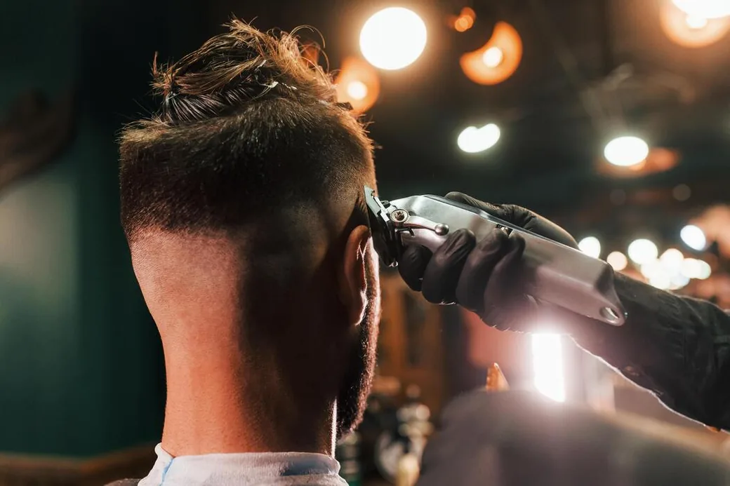 Barber running a cordless clipper up the neck during a low fade haircut